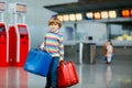 Cute little kid boy with luggage, two suitcases on international airport. Mother with little girl daughter on background