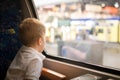 Cute little kid boy in a white t-shirt looking at the city out of the train window.  Child travelling by railway. young traveler Royalty Free Stock Photo