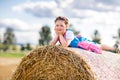 Cute little kid girl in traditional Bavarian costume in wheat field. German child with hay bale during Oktoberfest in