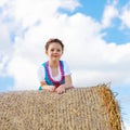 Cute little kid girl in traditional Bavarian costume in wheat field. German child with hay bale during Oktoberfest in