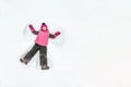 Cute little kid girl in warm ski sport suit making snow angel outdoors. Kid having fun lying on snowdrift after snow