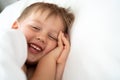 Cute little kid laughing to the camera, lying in bed. Royalty Free Stock Photo