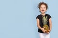 Cute little laught girl holding a pineapple, over blue background, studio shoot. Space for text.