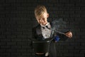 Cute little magician showing trick with hat against dark brick wall Royalty Free Stock Photo