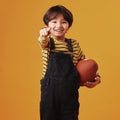 Cute little mixed race boy smiling and pointing while holding a football and posing against an orange copyspace Royalty Free Stock Photo