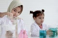 Cute little Muslim girls in lab coat wearing hijab scarf and doing experiment together with her friend, young scientist kid