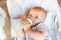 Cute little newborn girl drinking milk from bottle and looking at camera on white background. Infant baby sucking eating Royalty Free Stock Photo