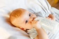 Cute little newborn girl drinking milk from bottle and looking at camera on white background. Infant baby sucking eating Royalty Free Stock Photo