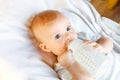 Cute little newborn girl drinking milk from bottle and looking at camera on white background. Infant baby sucking eating Royalty Free Stock Photo