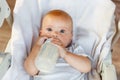 Cute little newborn girl drinking milk from bottle and looking at camera on white background. Infant baby sucking eating Royalty Free Stock Photo