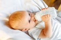 Cute little newborn girl drinking milk from bottle and looking at camera on white background. Infant baby sucking eating Royalty Free Stock Photo