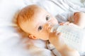 Cute little newborn girl drinking milk from bottle and looking at camera on white background. Infant baby sucking eating Royalty Free Stock Photo