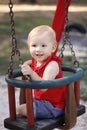 Baby girl smiling and sitting on the swing in the park
