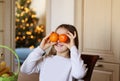 Cute little playful funny girl having fun holding orange tangerines in front of her eyes