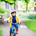 Cute little preschool kid boy riding on bicycle in park. Child in helmet, yellow rain coat and red rubber boots having Royalty Free Stock Photo