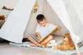 Cute little preschooler boy reading book to his toys sitting in cozy kids teepee tent in the living room at home Royalty Free Stock Photo