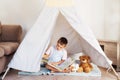 Cute little preschooler boy reading book to his toys sitting in cozy kids teepee tent in the living room at home Royalty Free Stock Photo