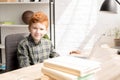 cute little redhead boy smiling at camera while sitting at table with books Royalty Free Stock Photo