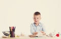 Cute little school boy with huge smile sitting at his desk on white background. Happy intelligent children in shirt with blue eyes