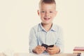 Cute little school boy with huge smile sitting at his desk on white background. Happy intelligent children in shirt with blue eyes Royalty Free Stock Photo