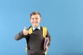 Cute little schoolboy with backpack showing thumb-up on color background Royalty Free Stock Photo