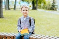 Cute little schoolboy sitting on bench in park outdoors autumn day. Young student with his backpack and books. Education Royalty Free Stock Photo