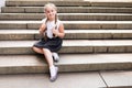 Cute little schoolgirl with bagpack sitting on large stone stairs on warm day