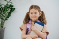 Cute little schoolgirl with purple backpack holding her books. White background Royalty Free Stock Photo