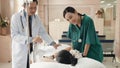 Cute little sick girl patient lying in hospital bed talking with smiling doctor and nurse standing at hospital Royalty Free Stock Photo