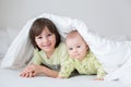 Cute little six month old baby boy and his older brother, playing under duvet at home in bed in bedroom, smiling Royalty Free Stock Photo