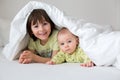 Cute little six month old baby boy and his older brother, playing under duvet at home in bed in bedroom, smiling Royalty Free Stock Photo