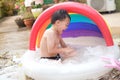 Cute Asian 5 boy child having fun splashing in inflatable swimming pool, playing alone at home