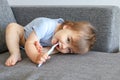 Cute little smiling baby boy holding toothbrush in his mouth and cleaning his first teeth lying in funny pose on the sofa looking Royalty Free Stock Photo