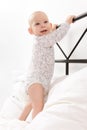 Cute little smiling baby boy infant standing on parent`s bed, holding onto the headboard. First attempts to stand up. Royalty Free Stock Photo