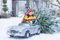 Cute little smiling kid boy driving vintage toy car with Christmas tree. Happy child in winter fashion clothes bringing Royalty Free Stock Photo