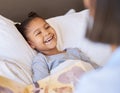 A cute little smiling mixed race girl laughing while lying in bed and enjoying story time. Young mother reading her Royalty Free Stock Photo