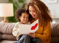 Cute little son giving his mom greeting postcard on Mothers day, celebrating together at home