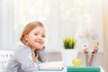Cute little student girl sitting at the table and looking into the camera. Sunlight from the window. Blurred background. Royalty Free Stock Photo