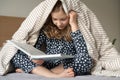 Cute teen child girl sitting and reading book on bed under the blanket