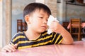 Cute little Thai boy with a severe runny nose wiping his snot with a paper handkerchief