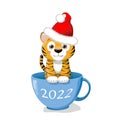 cute little tiger in a Santa hat is sitting in a blue cup. Cartoon New Year\'s clip art