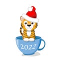 cute little tiger in a Santa hat is sitting in a blue cup.