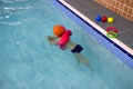 Cute little toddler boy child kicking feet in swimming costume use pool noodle and kickboard learn to swim at indoor Royalty Free Stock Photo