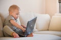 Cute little toddler boy sitting on the sofa with his laptop and looking at the window. Learning with computer. Early development. Royalty Free Stock Photo