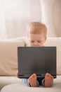 Cute little toddler boy sitting on the sofa with his laptop and looking at the window. Learning with computer Royalty Free Stock Photo