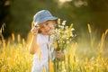 Cute little toddler child, blond boy, eating watermelon in beautiful daisy field