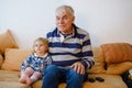 Cute little toddler girl and grandfather watching together tv show. Baby granddaughter and happy retired senior man