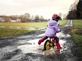 Cute little toddler girl with helmet riding on run balance bike through mud and puddles. Happy child having fun with Royalty Free Stock Photo