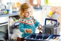 Cute little toddler girl helping in the kitchen with dish washing machine. Happy healthy blonde child sorting knives Royalty Free Stock Photo