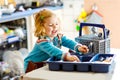 Cute little toddler girl helping in the kitchen with dish washing machine. Happy healthy blonde child sorting knives Royalty Free Stock Photo